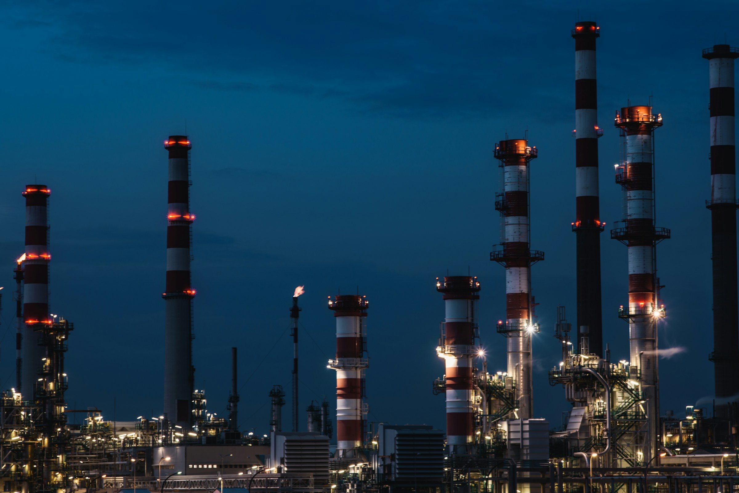 Refinery towers lit at night, illustrative